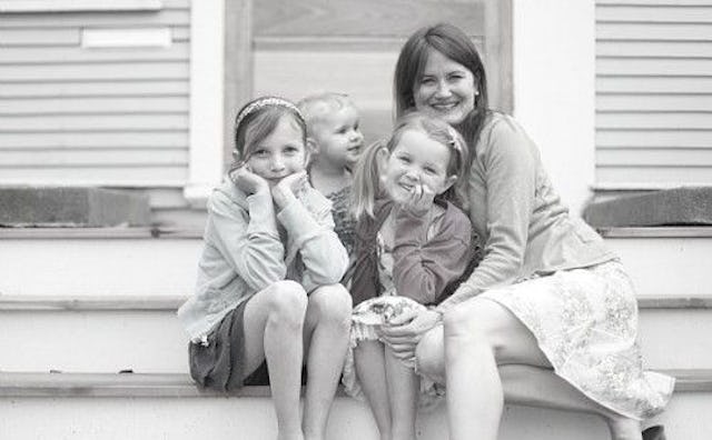 An older mother and her three daughters posing and smiling while sitting on a porch. 