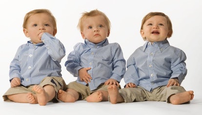 Blonde triplets sitting in light blue shirts and beige cargo trousers