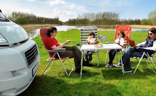 A family of four sitting on folding chairs in front of an RV they rented for a week for their trip