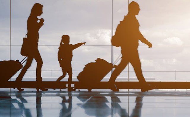 A silhouette of two people and a kid at the airport dragging their luggage