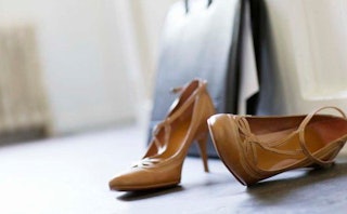 Brown heels standing on a black surface in the room next to the black bag