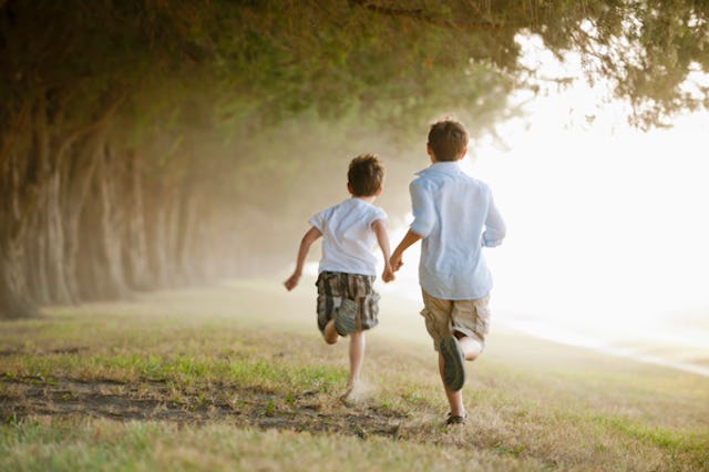 Two boys running through orchard while holding hands