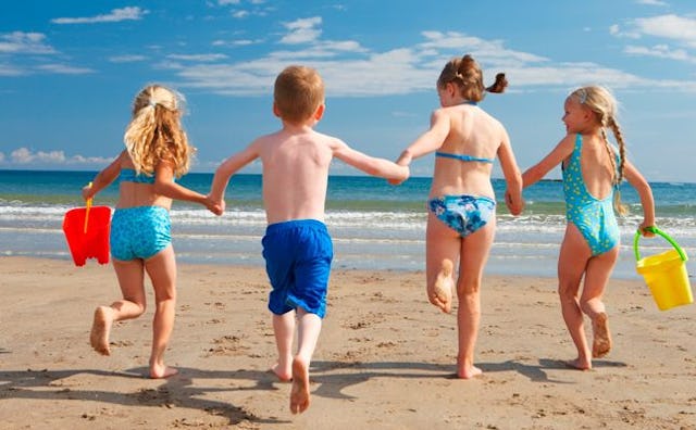 Three girls and a boy in bathing suits at the beach running towards the sea