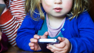 A toddler in a blue sweater using a touchscreen phone