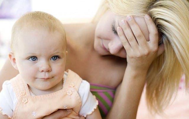 A blonde mom of a young blonde kid in her lap while holding her head down