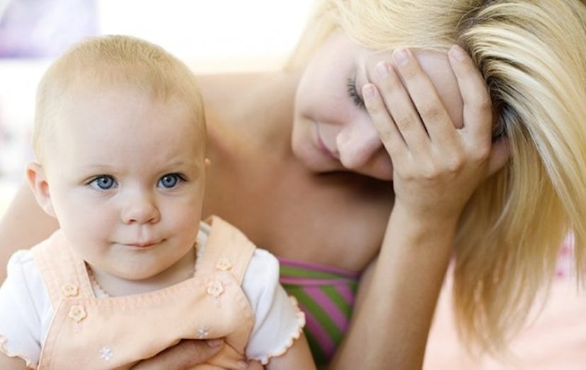 A blonde mom of a young blonde kid in her lap while holding her head down