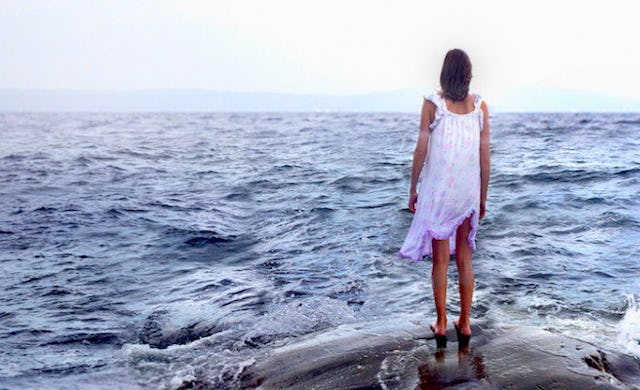 A woman in a white dress standing alone on a rock next to the ocean