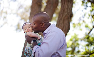 A man in a blue shirt, holding and kissing his baby daughter on the cheek
