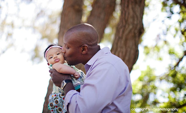 A man in a blue shirt, holding and kissing his baby daughter on the cheek