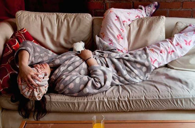 A pregnant woman wearing a gray robe and pajama, holding a head-cooling ice bag while lying on a cou...