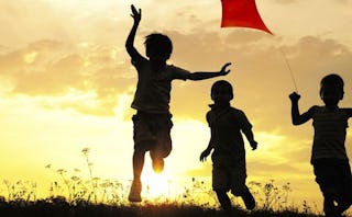 Three boys running with a kite during the sunset