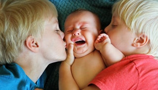 Two blonde boys kissing their baby brother on each cheek while he's crying