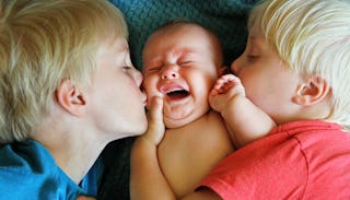 Two blonde boys kissing their baby brother on each cheek while he's crying