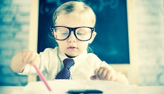 A child with large glasses in a bow tie drawing something.