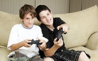Two boys playing video games on a beige couch, smiling 