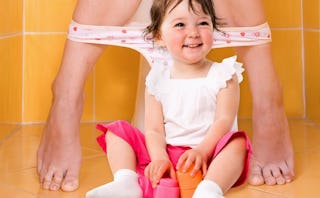 Woman sitting on the toilet with orange tiles and her daughter playing with toys in front