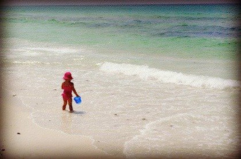 A toddler wearing a pink swimsuit and a matching hat on a sandy beach in Seagrove 