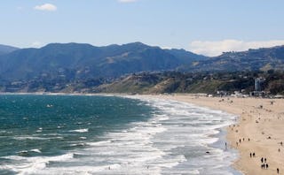 A panorama of a beach in Santa Monica, showing people on the sand beach, a restless sea, and mountai...