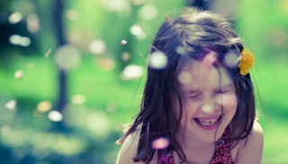 Little girl laughing with a yellow dandelion in her hair 