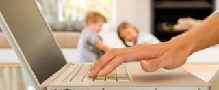 A close-up of the blogger's hands tapping on a grey laptop with two blurred kids in the background.