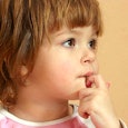An anxious little girl with a short haircut looks to the side with her hand on her chin.
