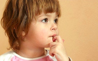 An anxious little girl with a short haircut looks to the side with her hand on her chin.