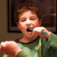 Mirror picture of a little boy brushing his teeth with a green toothbrush.