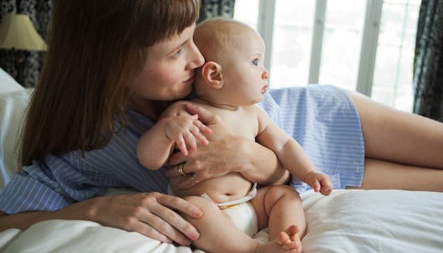 A joyful mother with brown hair, dressed in blue, reclining and tenderly kissing her baby.