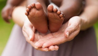 A mother's hands holding little feet of a newborn.
