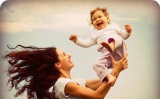 A happy mother in a white shirt holding her baby up with the blue sky in the background