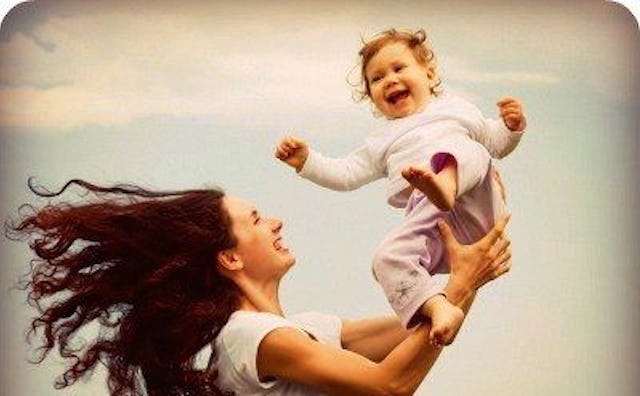 A happy mother in a white shirt holding her baby up with the blue sky in the background