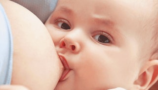 A close-up of a baby breastfeeding, looking straight at the camera