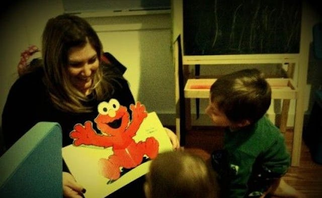 A mother holding a card with Elmo on it, smiling while showing it to her kids