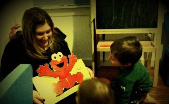A mother holding a card with Elmo on it, smiling while showing it to her kids 