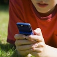 Young teen lying on the grass in a red t-shirt while texting on his phone
