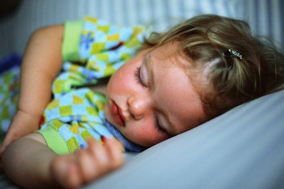 A baby sleeping peacefully in a blue/yellow/green shirt