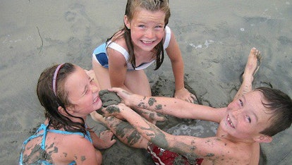 Three kids playing in the mud and having fun together.