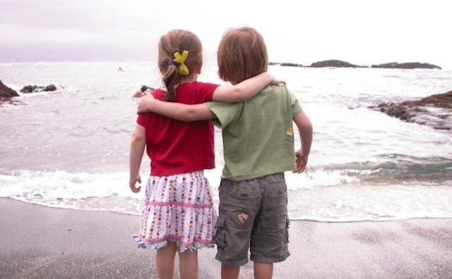 Two children, a boy and girl from the back hugging and looking at the sea