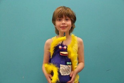 A boy in a yellow tank top holding a purple and yellow toy.