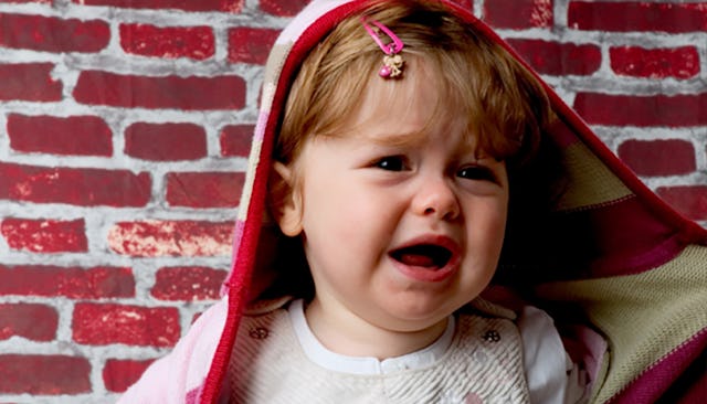 A little girl in a red jacket and a pink hair clip crying
