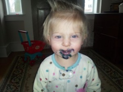 A young blonde child smiling while having black paint over her mouth 