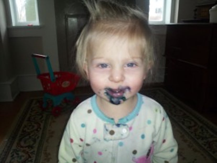 A young blonde child smiling while having black paint over her mouth 