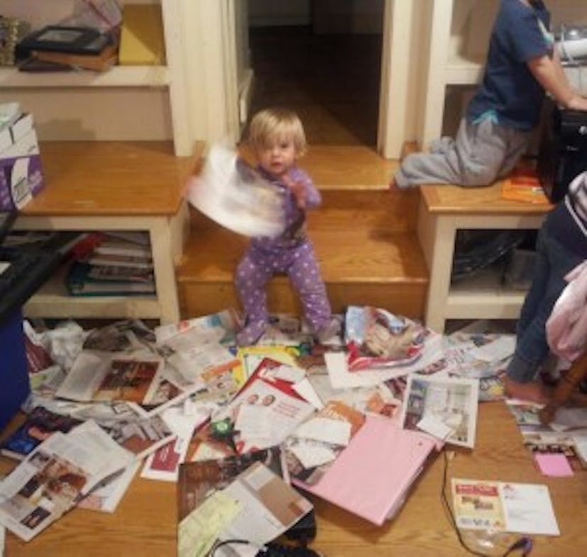 Two children making a mess with a lot of papers on the floor inside a room