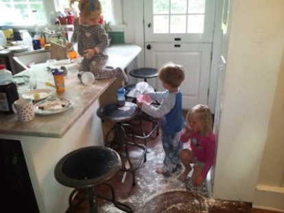 Three kids eating powdered sugar inside their messy kitchen in their house 