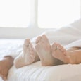 Two people lying on a white bed, covered with a white sheet while their feet are sticking out with t...