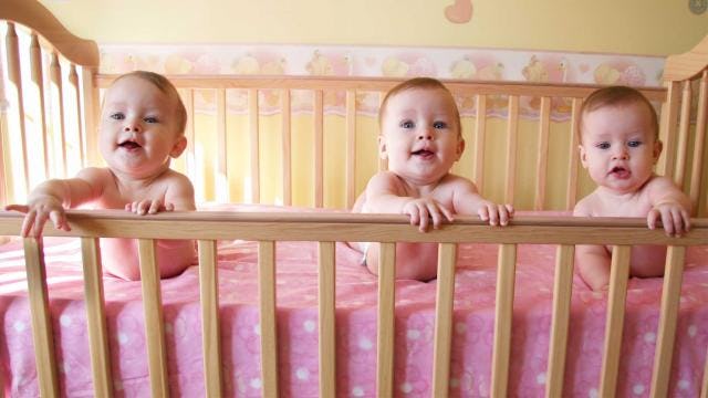 An adorable baby girl  triplet in a pink crib