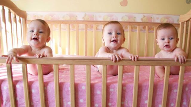 An adorable baby girl triplet in a pink crib