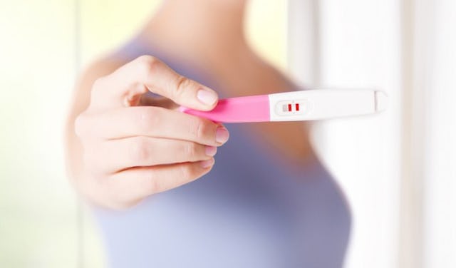 A close-up of a woman holding a white-pink pregnancy test
