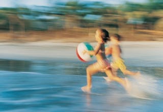 Two kids running down a sand beach into the sea