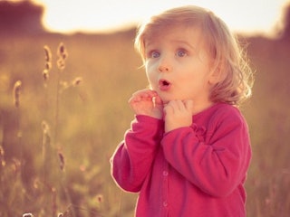 A girl wearing a pink button-up sweater, standing in the field with a surprised facial expression